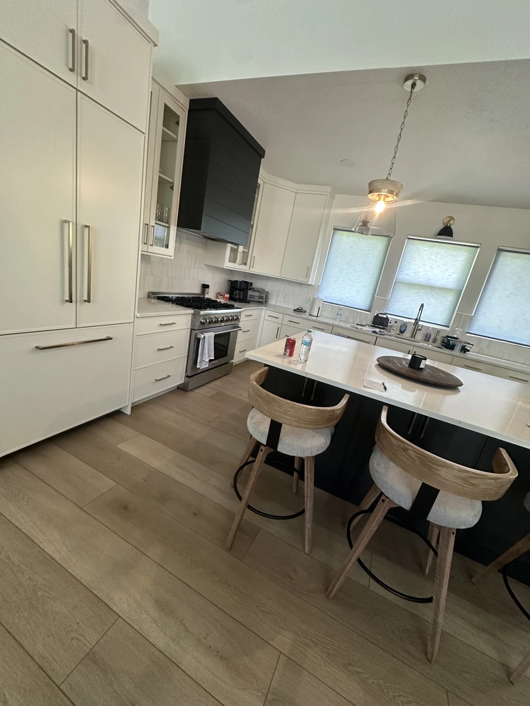 Remodeled kitchen in Ogden with white flat-panel cabinets, a black range hood, and a seated island on light oak plank flooring